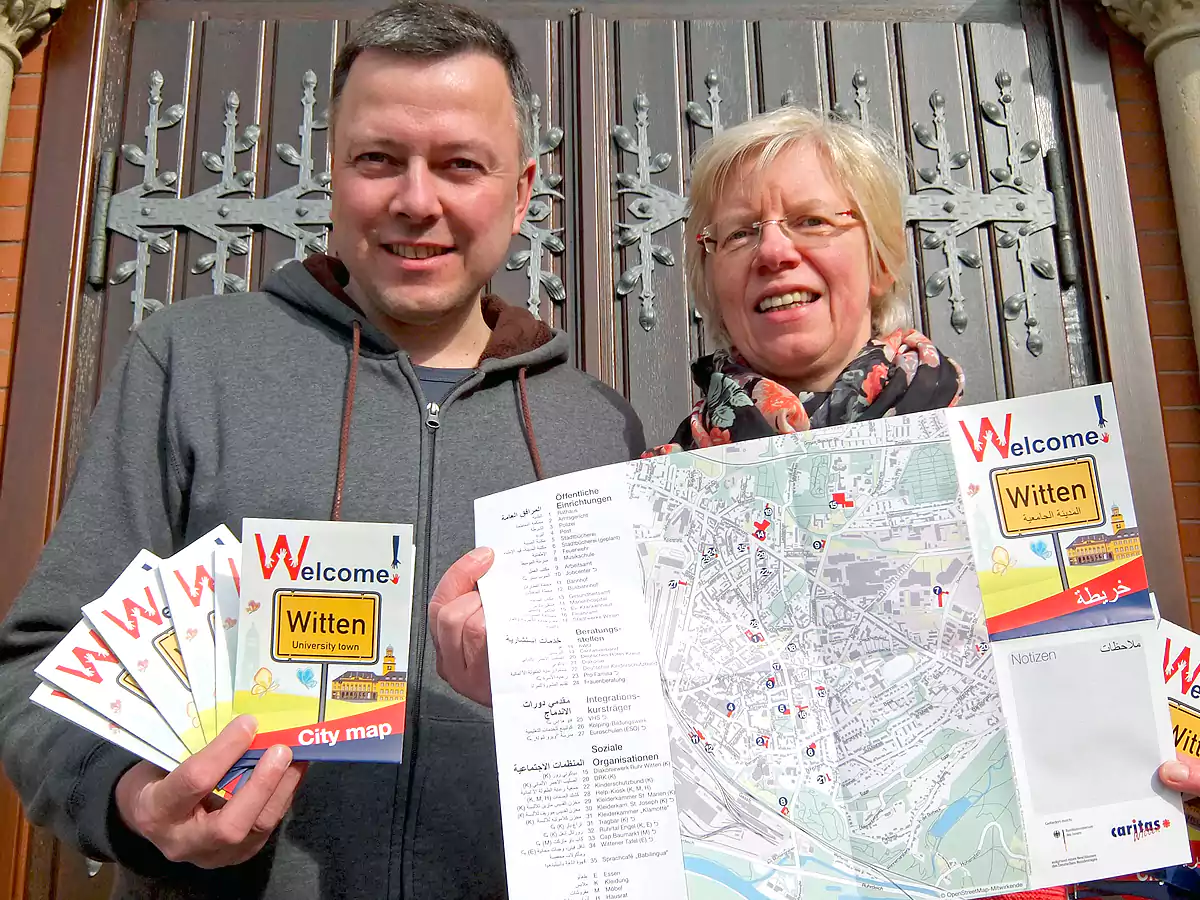 Wichtige Informationen und Organisationen werden in arabisch, englisch, deutsch und aufgeführt. Christine Henkel vor der Marien-Kirche und Marek Schirmer, Projektmitarbeiter beim Caritasverband präsentieren die neuen Wittener Stadtpläne.